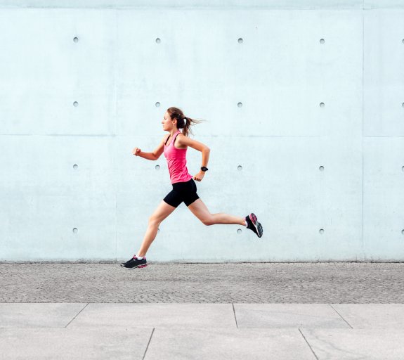 Sporty woman running in front of concrete wall 